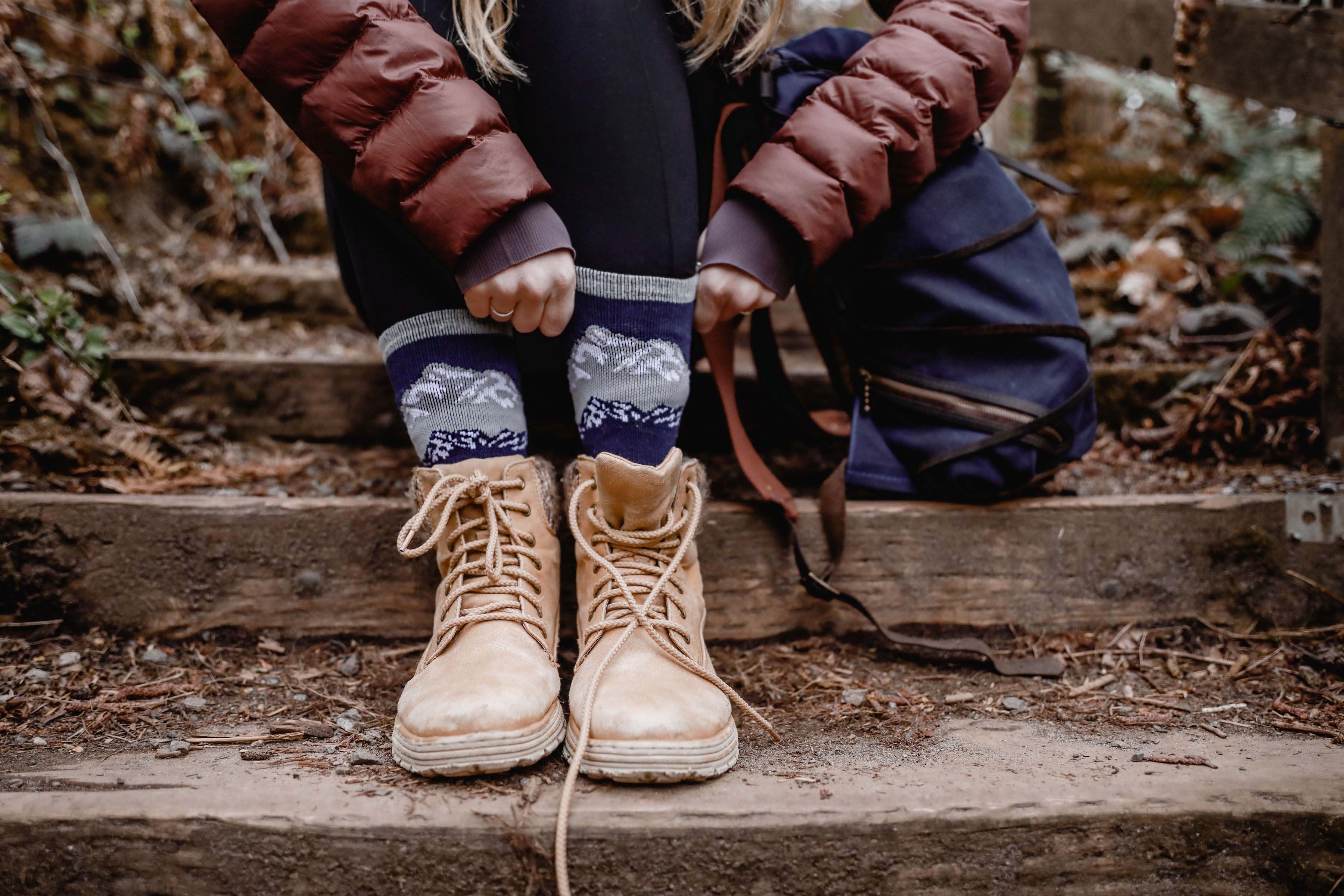 A woman is pulling up her merino wool socks as she prepares to tackle a trail.