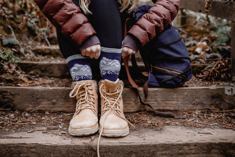 A woman is pulling up her merino wool socks as she prepares to tackle a trail.