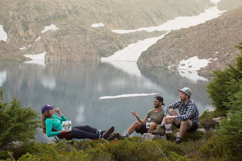 Two men and a woman lounge by a lake eating lunch.