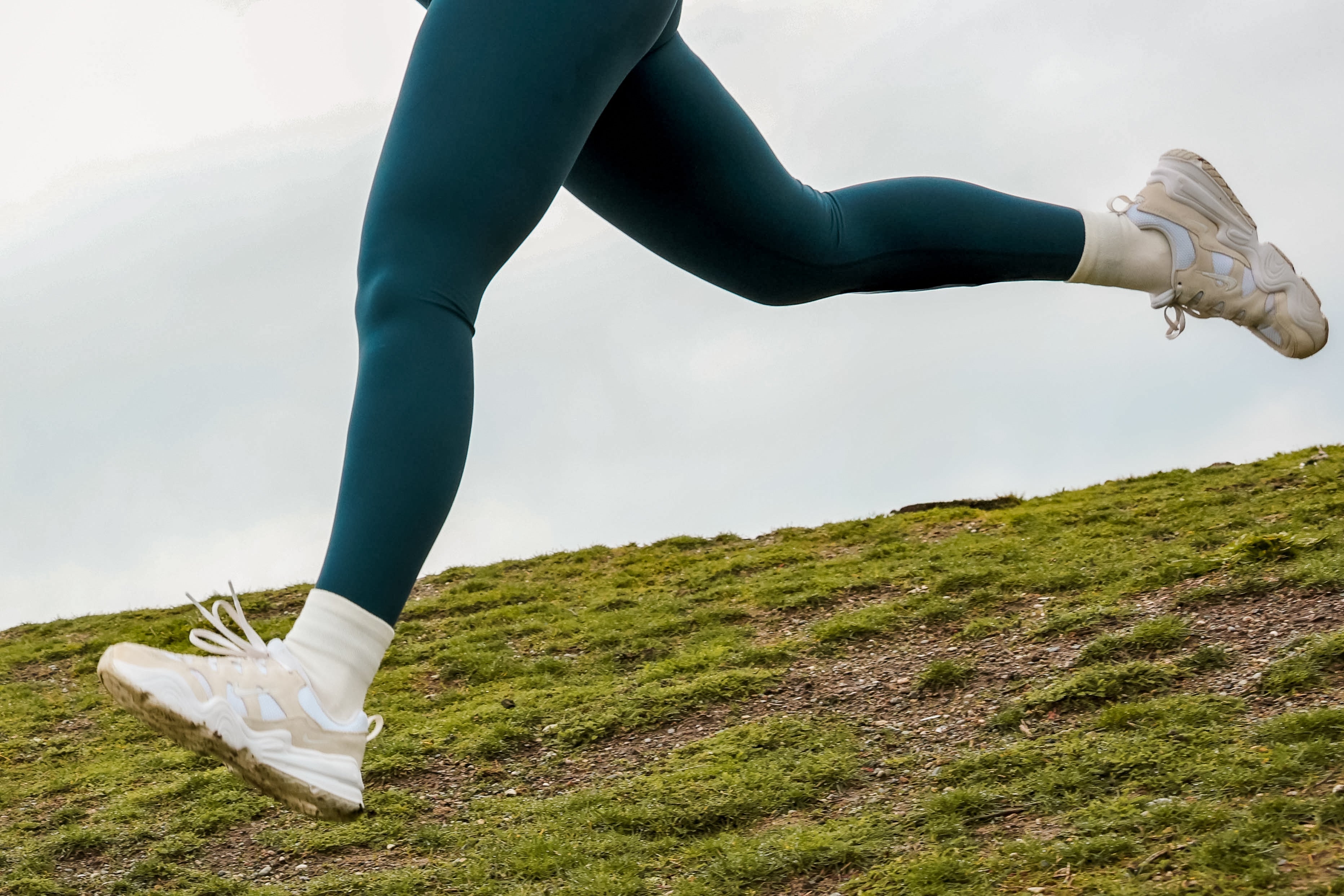 A person is running down a hill with the camera focused on their feet, wearing running shoes and merino wool socks.